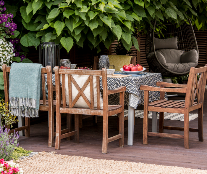 outdoor dining table and chairs made out of teak wood on a patio surrounded by plants and flowers