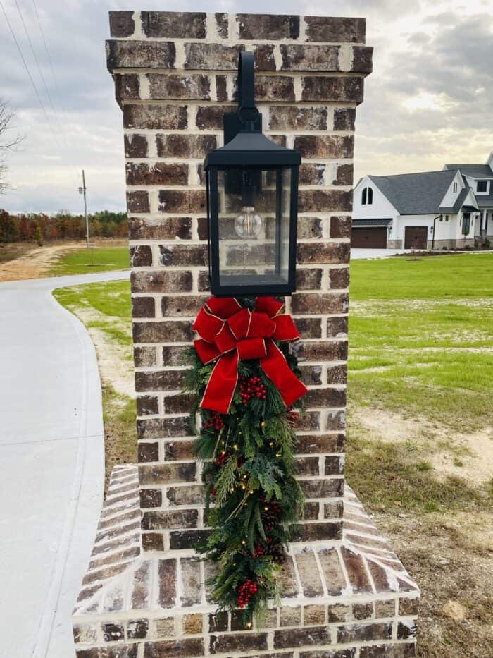 christmas swag on driveway column - greenery with berries, a bow and twinkle lights