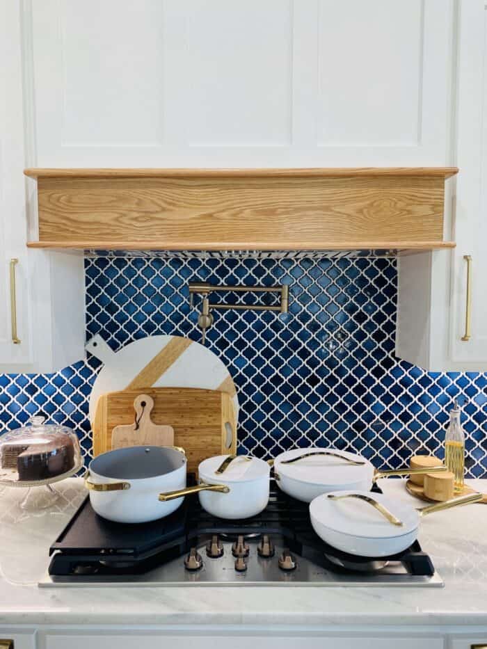 caraway cookware set on top of cooktop with navy and white tile backsplash